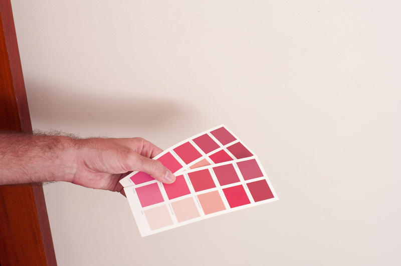 Man holding two red paint color charts against a white wall with swatches of various red hues as he makes a decision on his redecorating during renovations