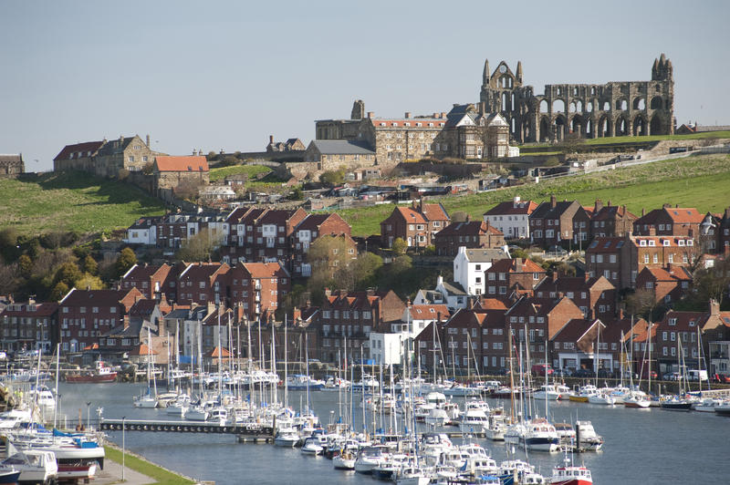 View of pleasure yachts moored at Whitby in the upper harbour with the abbey ruins visible on top of the hill overlooking the port