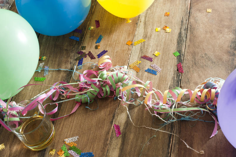 Party decoration background of tangled colorful streamers, balloons and scattered confetti on a wooden table with copyspace for your greeting or invitation