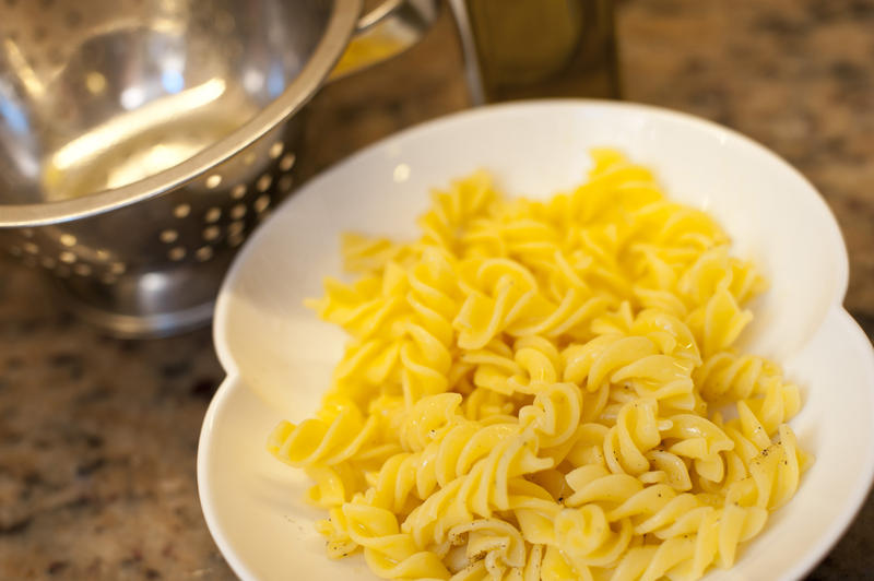 Bowl of plain cooked Italian fusilli pasta waiting to have a savory sauce added, high angle view with a metal colander