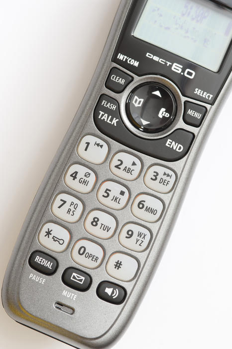 Telephone handset and receiver viewed from above showing the keypad with the numbers, letters, screen and functions on a white background