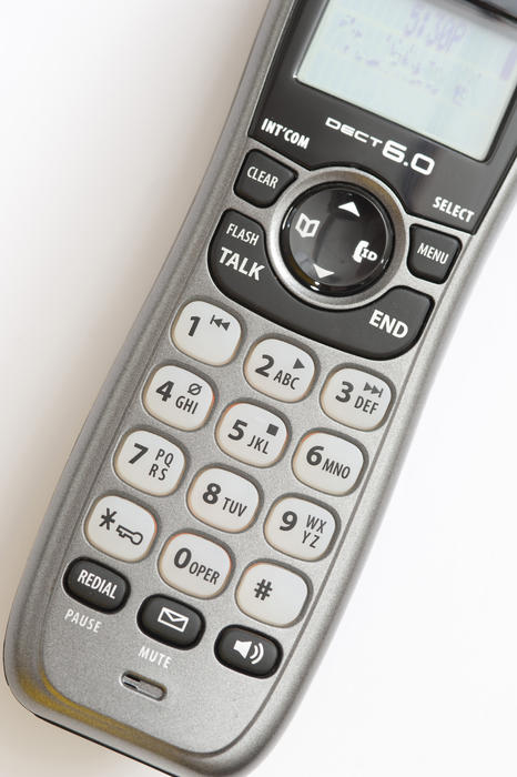 Telephone handset and receiver viewed from above showing the keypad with the numbers, letters, screen and functions on a white background