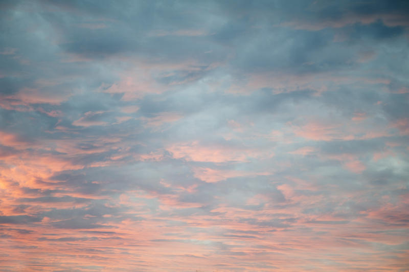 Delicate diffuse pink sunset lighting up a heavy cloud cover from below as the sun sinks below the horizon in a cloudscape and nature background