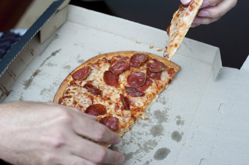 Hands of a man eating a slice of a takeaway pepperoni pizza still in its traditional cardboard box