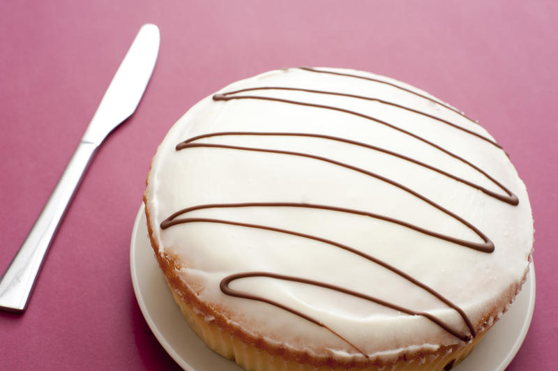 Plain iced cake with a zigzag pattern on the icing and knife alongside to cut it over a red background