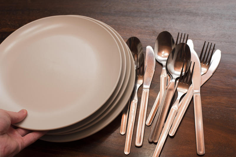 Man taking an empty plate on a buffet table from a stack of white plates alongside a pile of silver cutlery