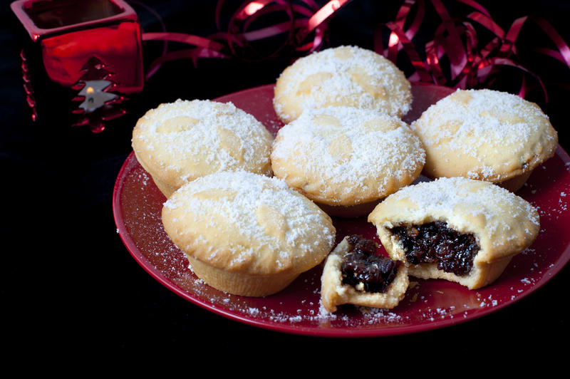 Plate of freshly baked Christmas mince pies with one broken open to display the rich fruity filling