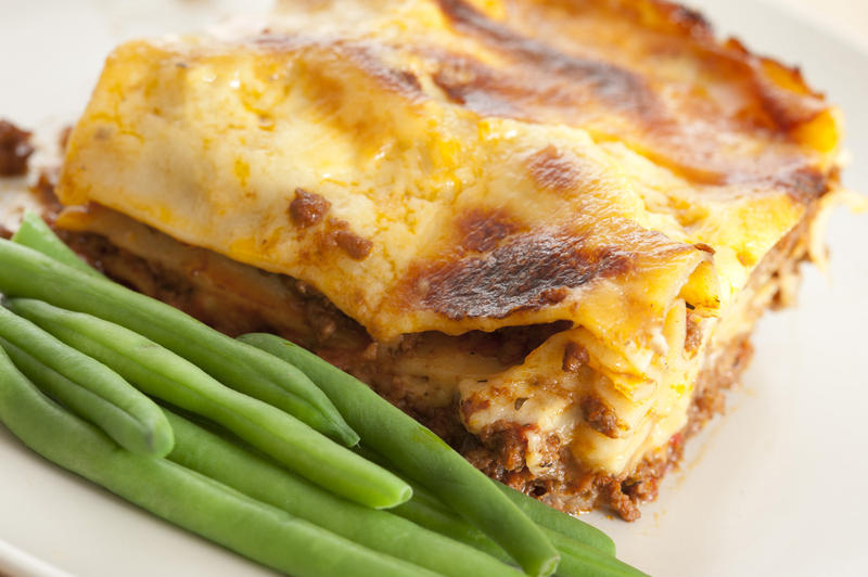 Close up Tasty Lasagna Recipe with Green String Beans on the Side, Served on White Plate.