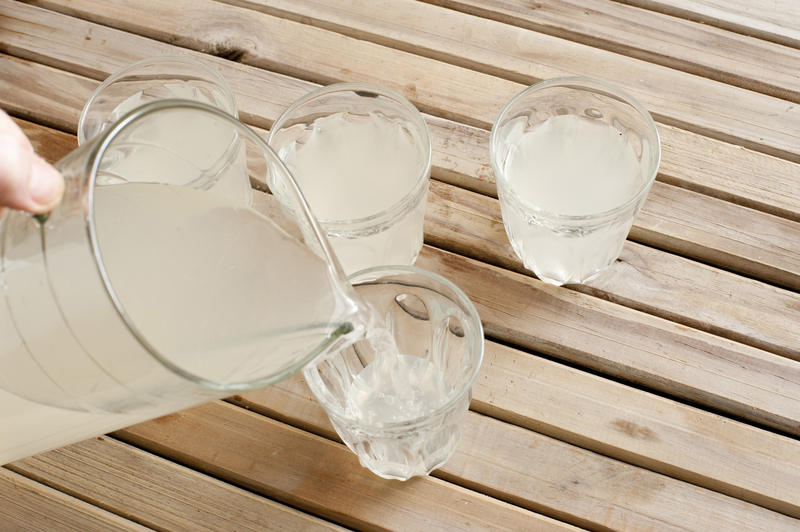 Man pouring refreshing homemade lemonade from a large jug into tumblers on a summer picnic table, high angle view