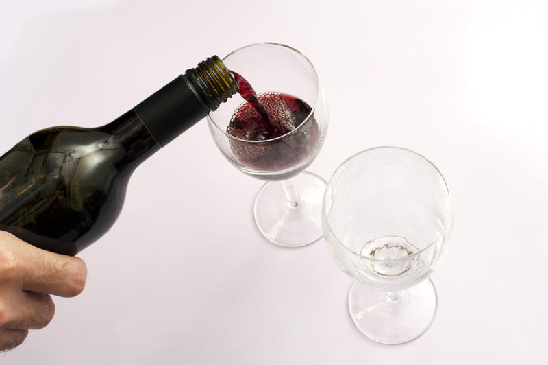 Man or wine steward in a restaurant serving two glasses of red wine pouring it from an unlabeled bottle, view from overhead on white