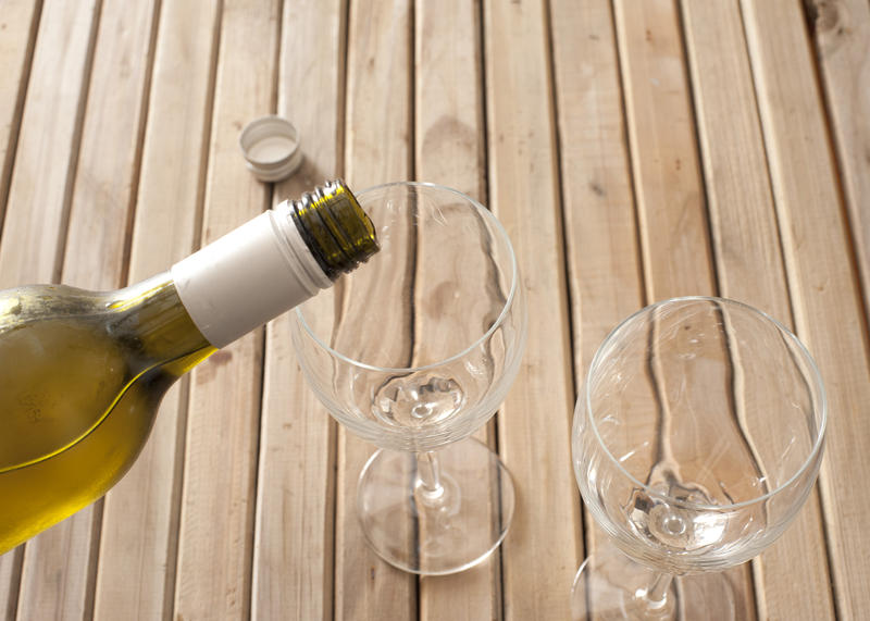 Pouring white wine from a bottle into two empty wine glasses, close up view of the top half of the bottle and glasses on a wooden slatted table with copyspace