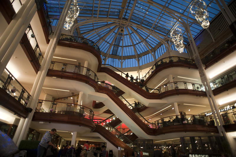Interior of the shopping mall at the Princes Square Shopping Centre, Glasgow with shoppers looking over the gallery and using the escalators between floors, illuminated at night