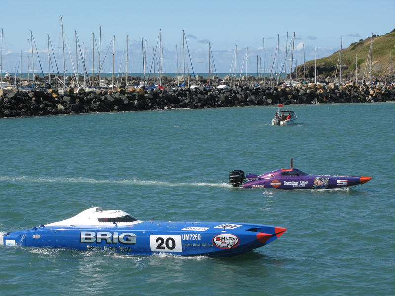 Competitors in a power boat race idling their craft before the start of the race with a breakwater and marina in the background