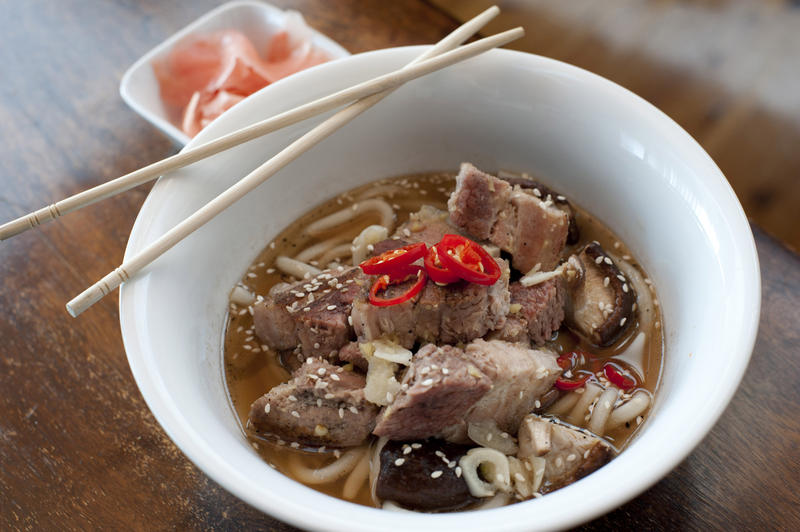 Japanese ramen, a traditional dish of noodles in broth, garnished with chunks of cooked pork and served in a bowl with chopsticks