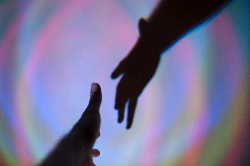 Silhouette of two hands reaching for each other in help, welcome or to shake hands against a colourful blurred background with circular motion effect