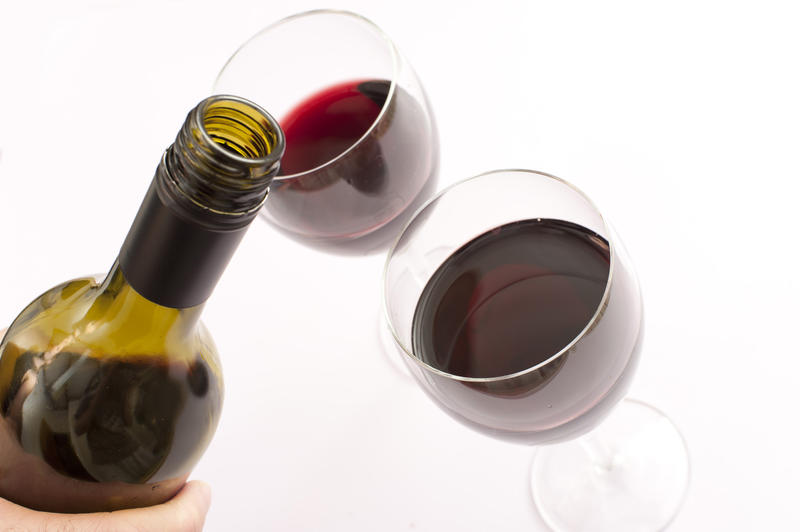 Closeup of the hand of a man pouring two glasses of red wine from an almost full unlabeled bottle in the foreground