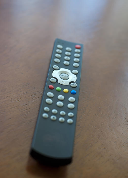 Universal remote control for controlling and changing the programs and audio on a television set lying on the brown fabric of a sofa