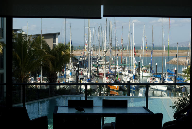 View from a patio with dining table of a holiday resort swimming pool and marina with moored yachts and pleasure boats