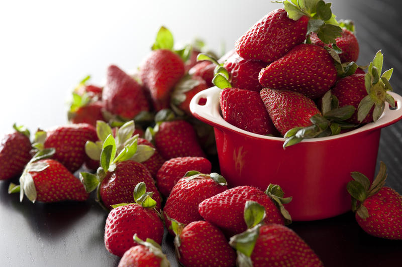 Freshly picked harvest of delicious ripe red juicy strawberries with green stalks overflowing from a small red bowl