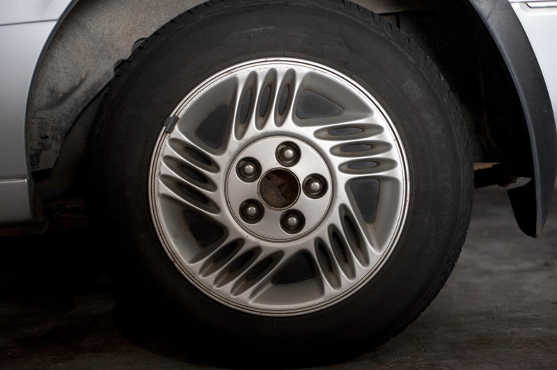 Car wheel with alloy silver sports rim parked on tarmac, close up side view
