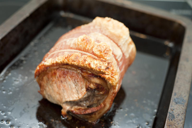 Crisp pork roast with crackling standing in its own juices in a roasting pan during cooking and preparation of a meal