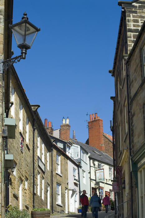 Pedestrians climbing the narrow steep Kings Street , Robin Hoods Bay, Yorkshire between traditional quaint stone cottages