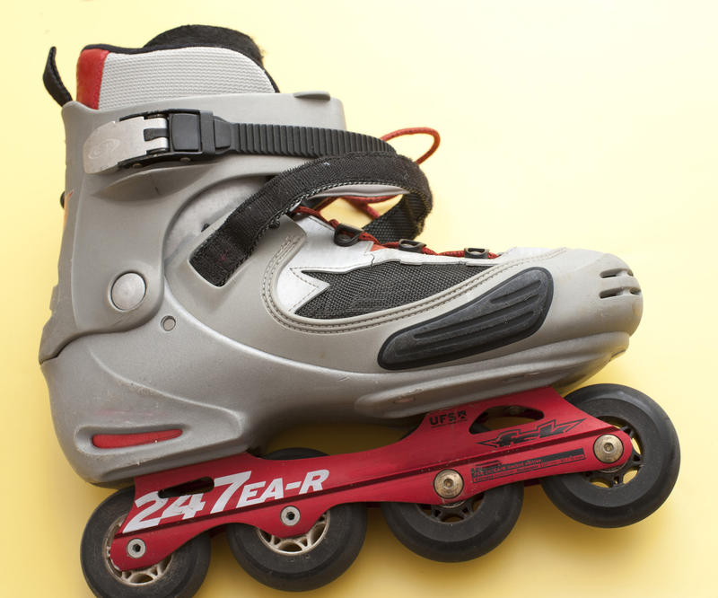 Single roller blade or skate with alighned wheels in a line lying on its side on a yellow background in a sport and exercise concept
