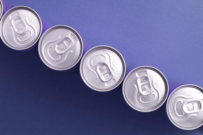 Row of beverage cans arranged in a diagonal line on a blue background, close up overhead view with copyspace