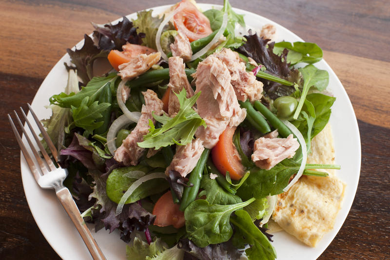 High angle view of fresh leafy green salad nicoise with herbs and olives topped with tuna and served on an egg omelette