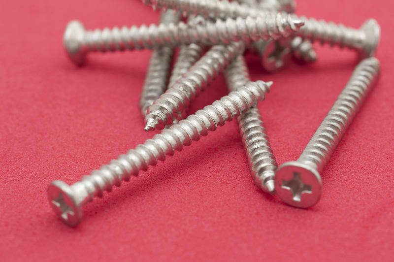 Pile of silver metal ful thread woodworking screws on a red background showing the Phillips head with copyspace