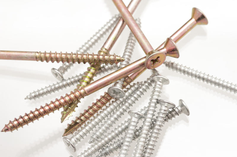 Assorted woodworking screws with both full thread and countersunk screws in a random heap in a white background