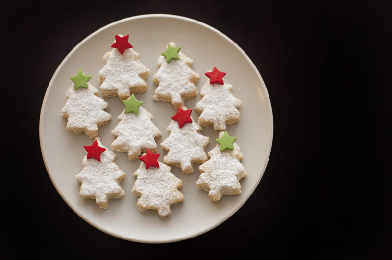 Decorative seasonal Christmas biscuits or cookies in the shape of Christmas trees with colourful stars arranged on a plate on a black background