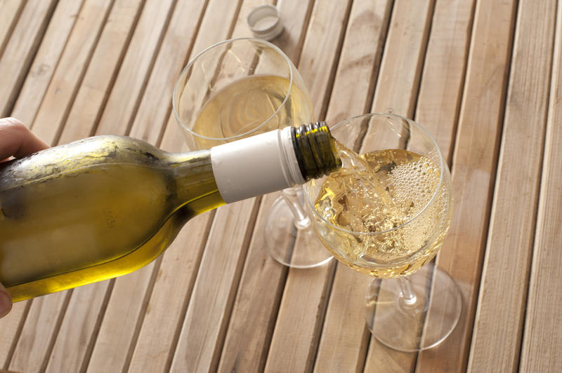High Angle Close Up View of Hand Pouring Glasses of White Wine from Chilled Green Wine Bottle on Wooden Picnic Table