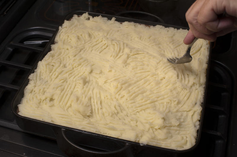 Cook preparing the Shepherds Pie potato topping marking a traditional pattern in the mashed potato with a fork before baking it in the oven