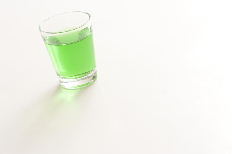 Shot glass of green absinthe, a green liqueur having a bitter anise or liquorice flavor and a high alcohol content, on a white background with copyspace