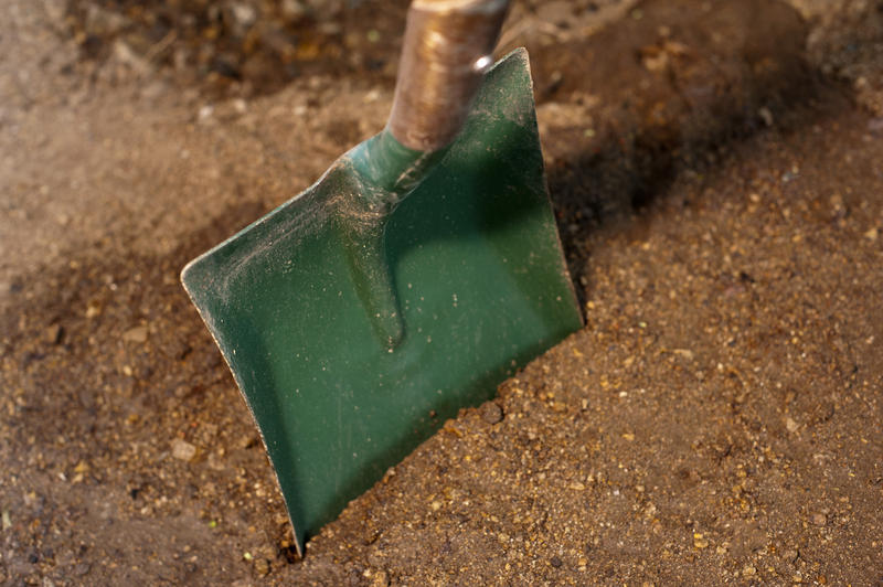 Green garden shovel standing upright in freshly prepared garden soil ready for the spring planting