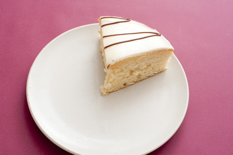 Single slice of freshly baked tasty cake with decorative icing on a plate over a deep pink background , high angle view