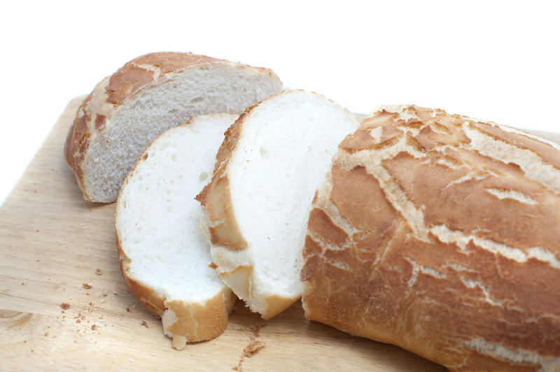 Sliced crispy freshly baked white bread baguette or roll on a bread board, close up view over white with copyspace