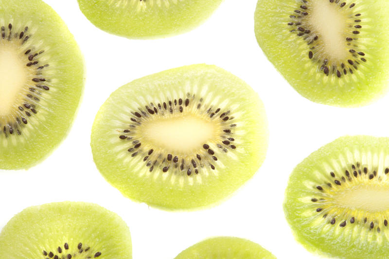 Thinly sliced and peeled exotic kiwifruit arranged on a white background for a decorative pattern showing the green flesh and ring of pips