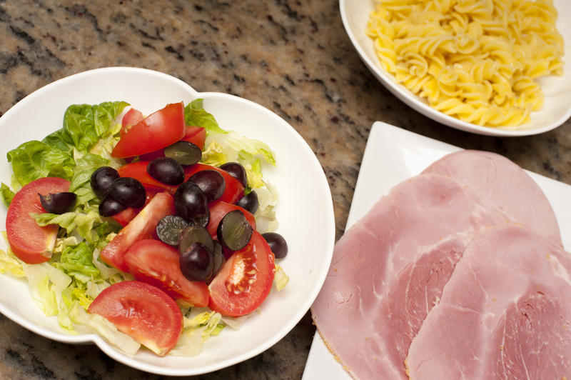 Overhead view of a plate of sliced cold ham and a side dish of fresh mixed Mediterranean salad with tomato, lettuce an olives