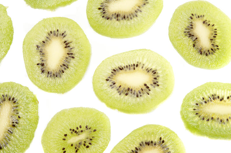 Pattern of fresh kiwifruit slices on a white background in a random arrangement showing the juicy green flesh and ring of pips