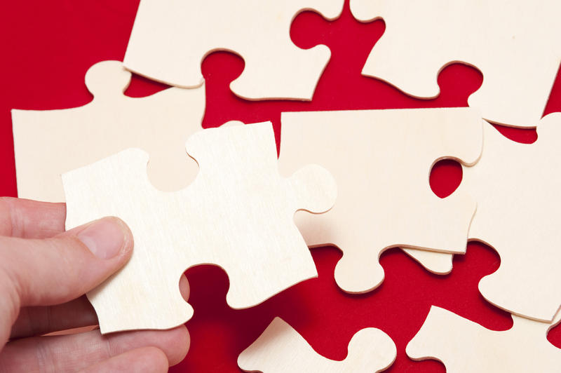 Man holding a jigsaw puzzle piece above several additional pieces on a red background in a problem solving concept