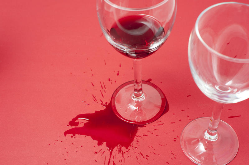 Spilled red wine around the foot of a wine glass splashed across a red party background, high angle with copyspace