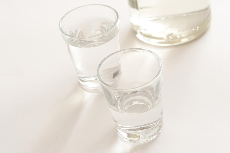 Two shot glasses of clear spirits served neat with the base of a bottle of alcohol visible behind, high angle view with copyspace