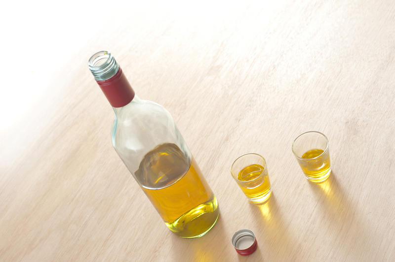 Uncork bottle of rum and two cups on wooden table