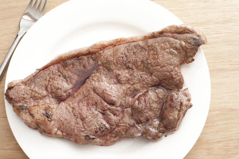 Roasted beefsteak on white plate and fork from above.