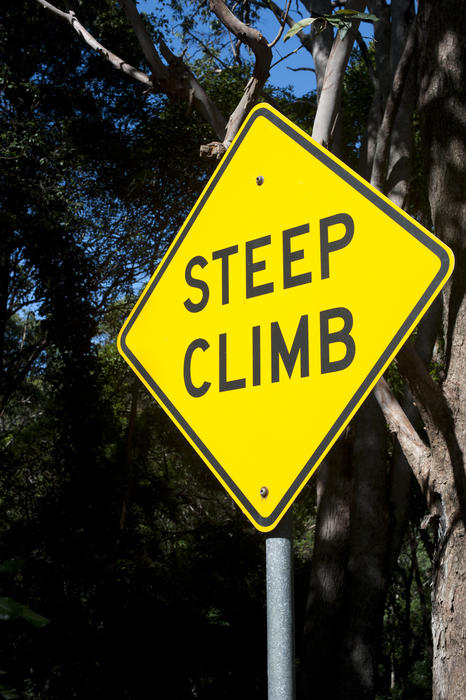 Close up Steep Climb Sign on a Yellow Diamond with Metal Bar Stand with Big Trees at the Background.