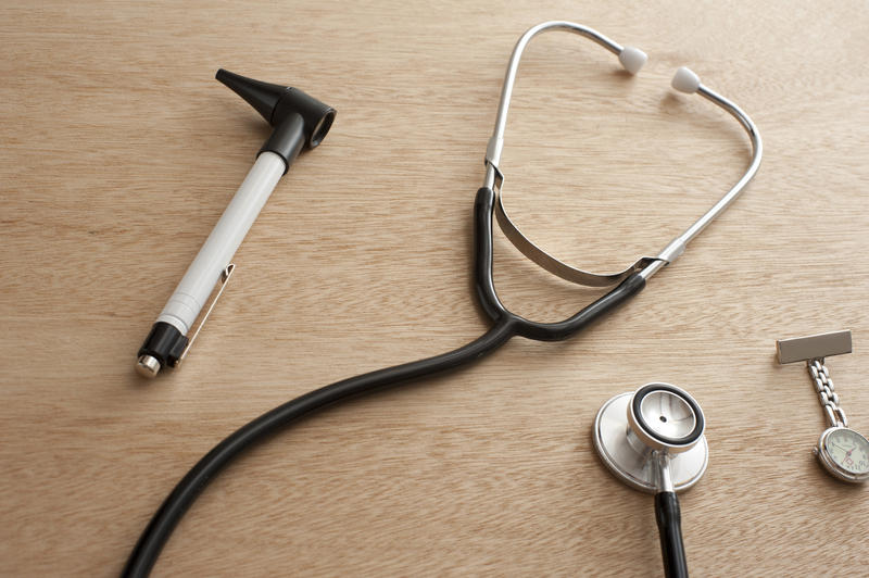 Otoscope, Stethoscope and Pocket Watch on Wooden Desk - Concept Image of Medical Supplies Scattered on Desk