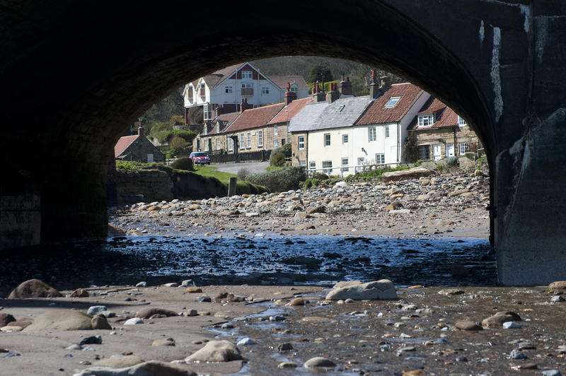 View through the arch of a stone bridge of quaint waterfront cottages at the coastal village of Sandsend