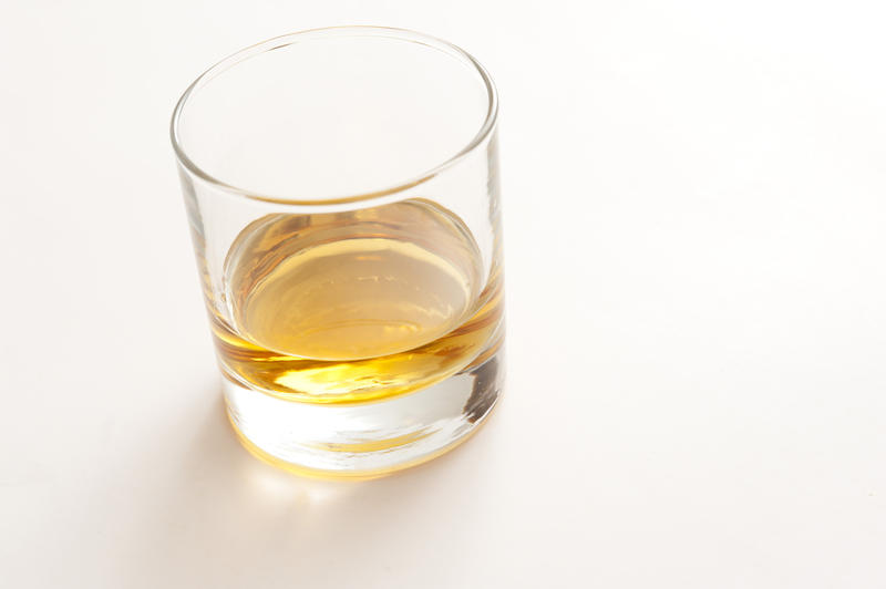 Tot of straight whiskey or scotch served neat in a plain glass tumbler on a white background with copyspace